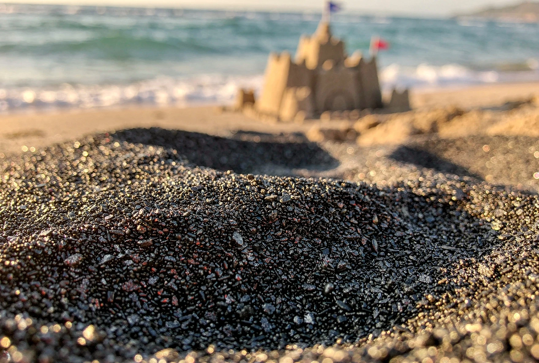 Fine black magnetic sand on Ureki beach with gentle waves and warm summer light