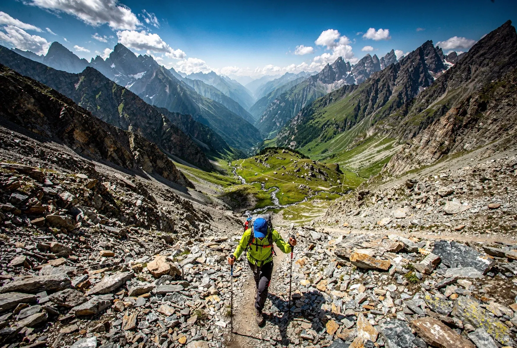 Hiker descending the steep rocky trail from Chaukhi Pass with dramatic valley and peaks in the background