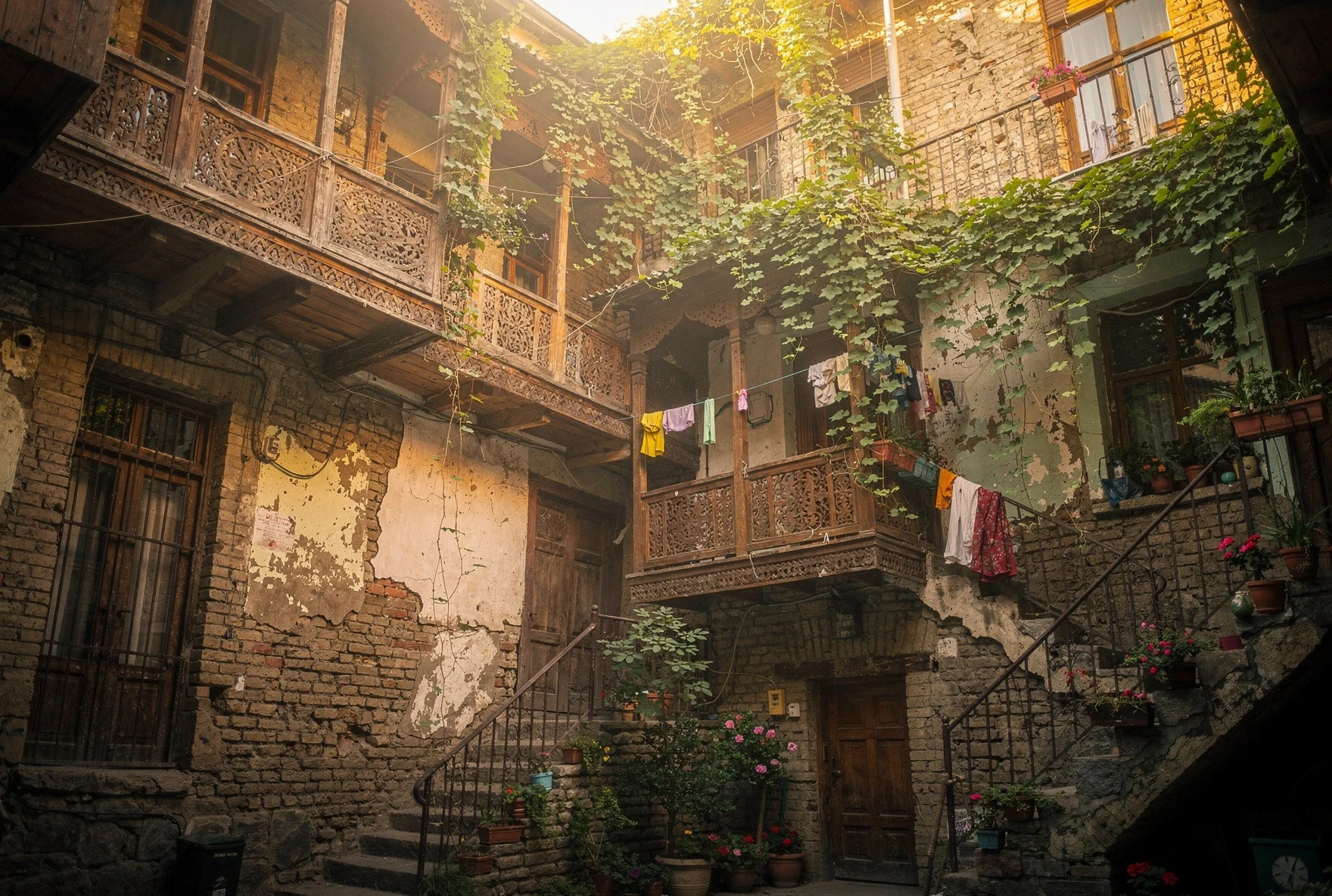 Traditional Tbilisi courtyard with ornate wooden balconies, grapevines, and warm golden sunlight filtering through
