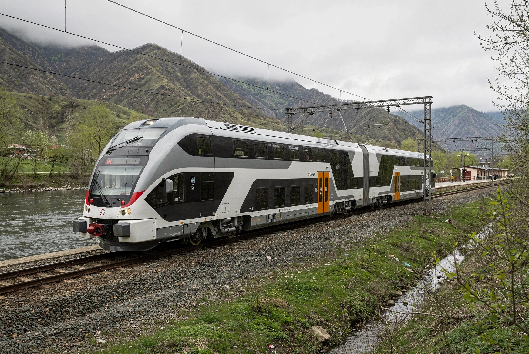 Double-decker passenger train traveling through a green Caucasus river valley in Georgia