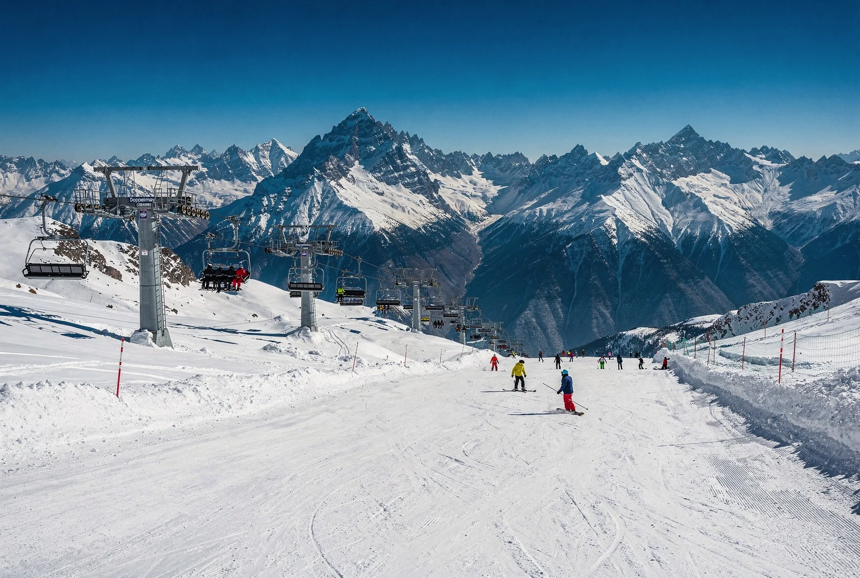 Skiers on the wide open groomed slopes at Gudauri with a chairlift and Caucasus mountain panorama behind them