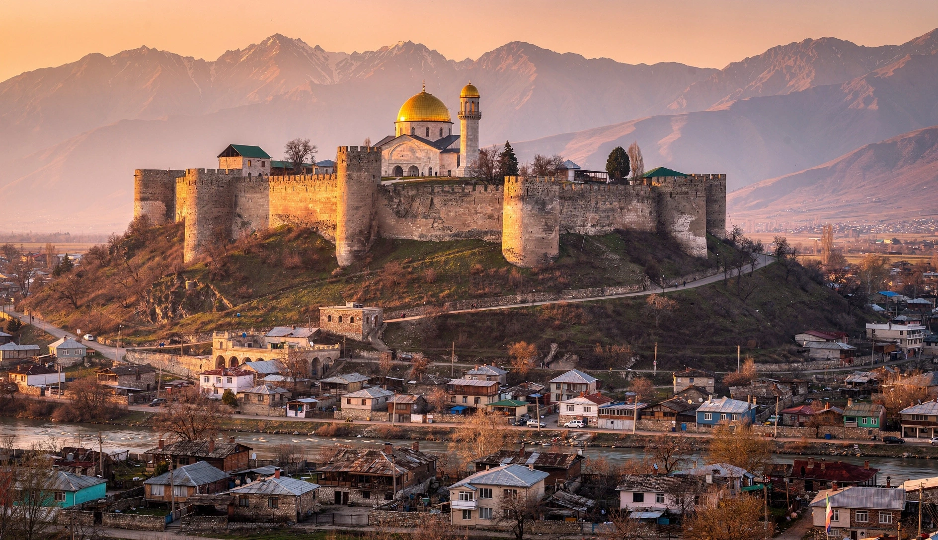 Panoramic view of a medieval fortress complex with a golden-domed mosque on a hilltop in southern Georgia at golden hour