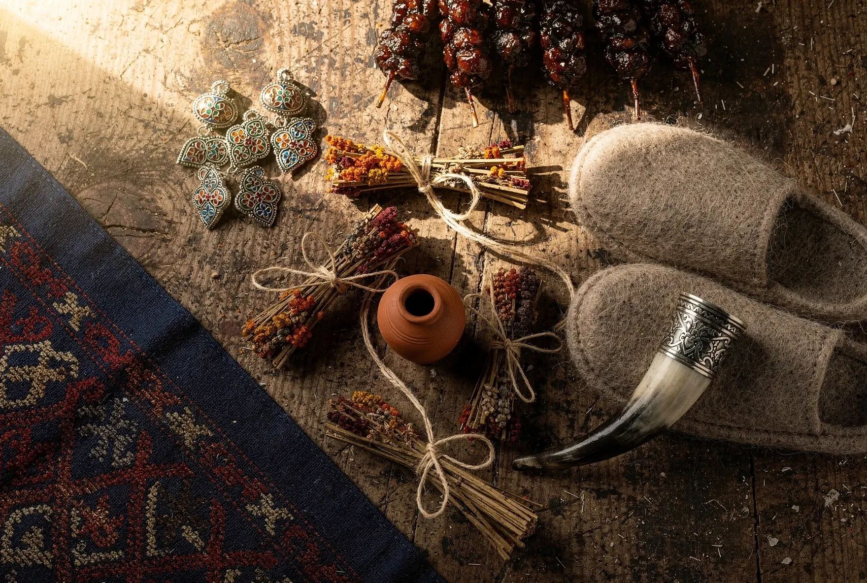 Georgian souvenirs and crafts arranged on a wooden table including enamel jewelry, churchkhela, and a drinking horn
