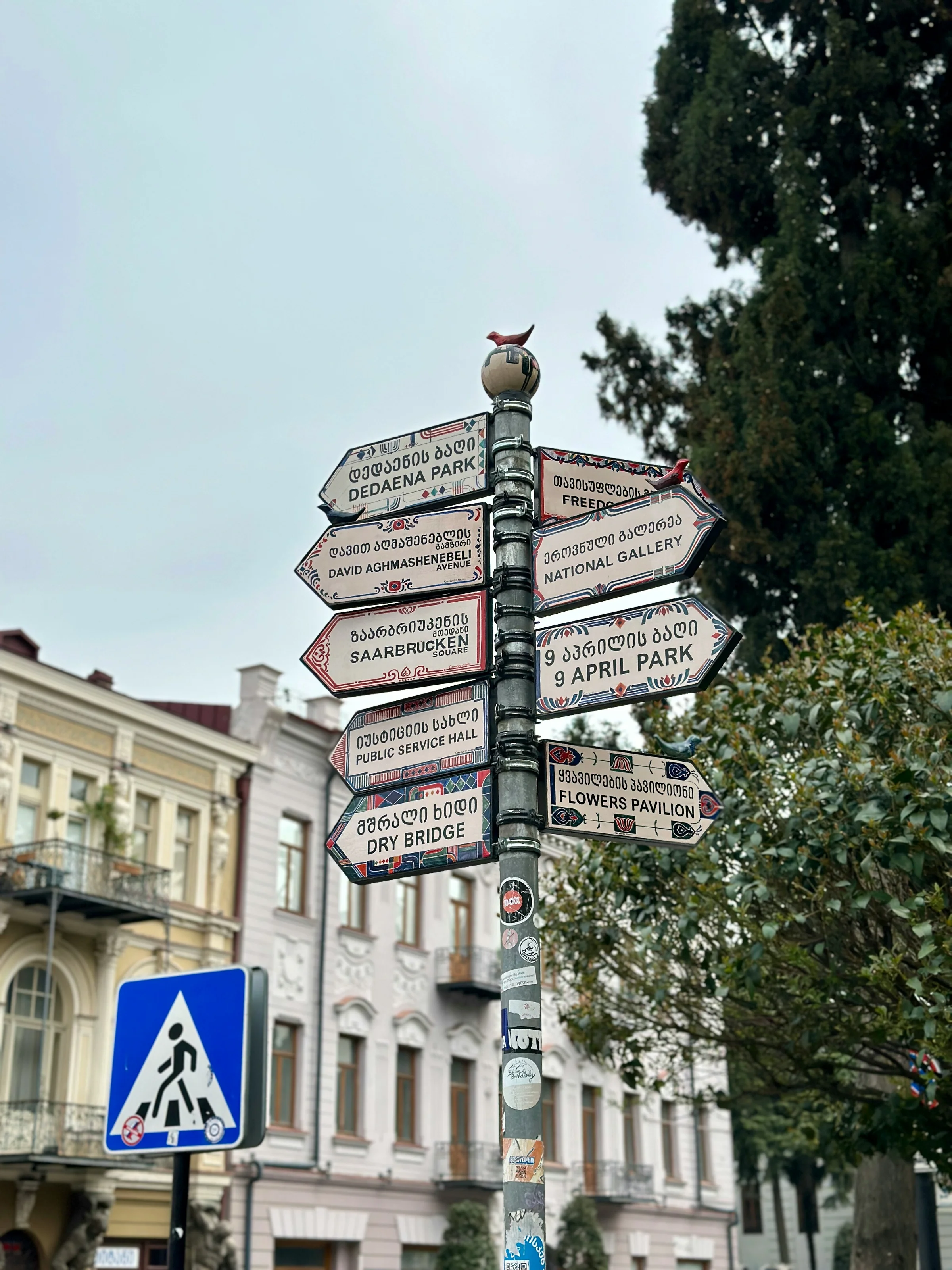 Directional signpost in Tbilisi with Georgian and English text pointing to landmarks