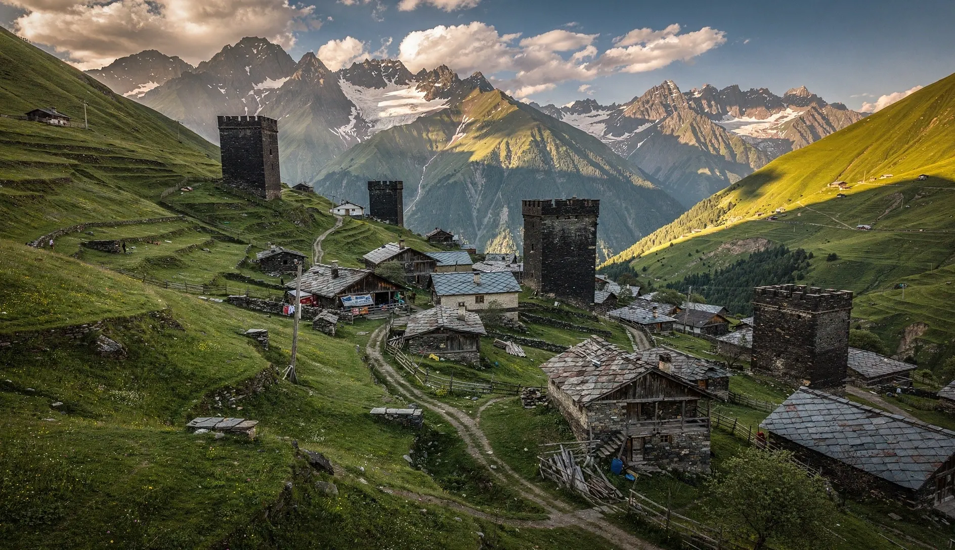Ancient stone defensive towers rising from a mountain valley in Tusheti, Georgia, with alpine meadows and Greater Caucasus peaks in the background