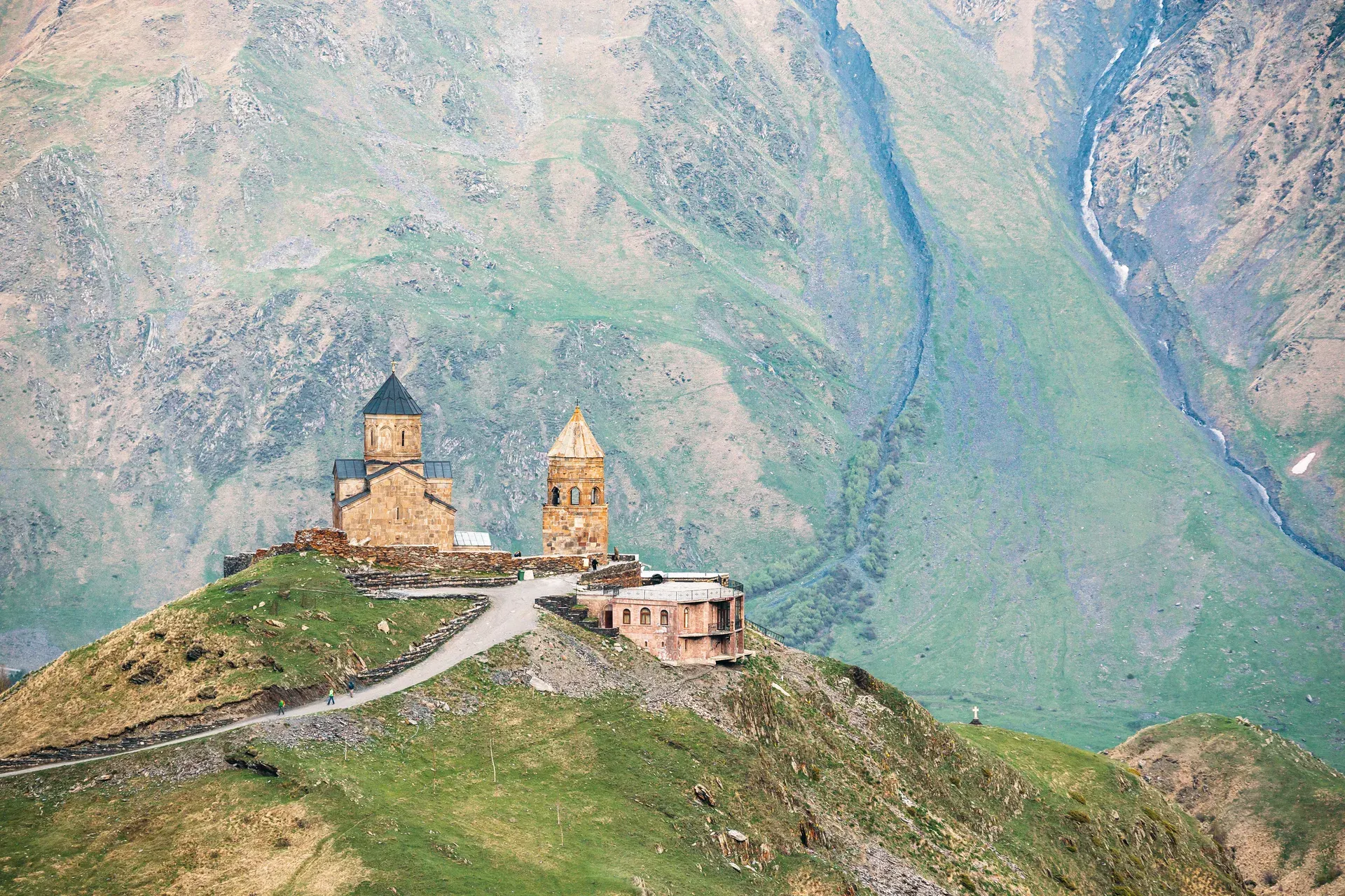 Gergeti Trinity Church perched on a hilltop with Mount Kazbek towering behind it against a dramatic sky