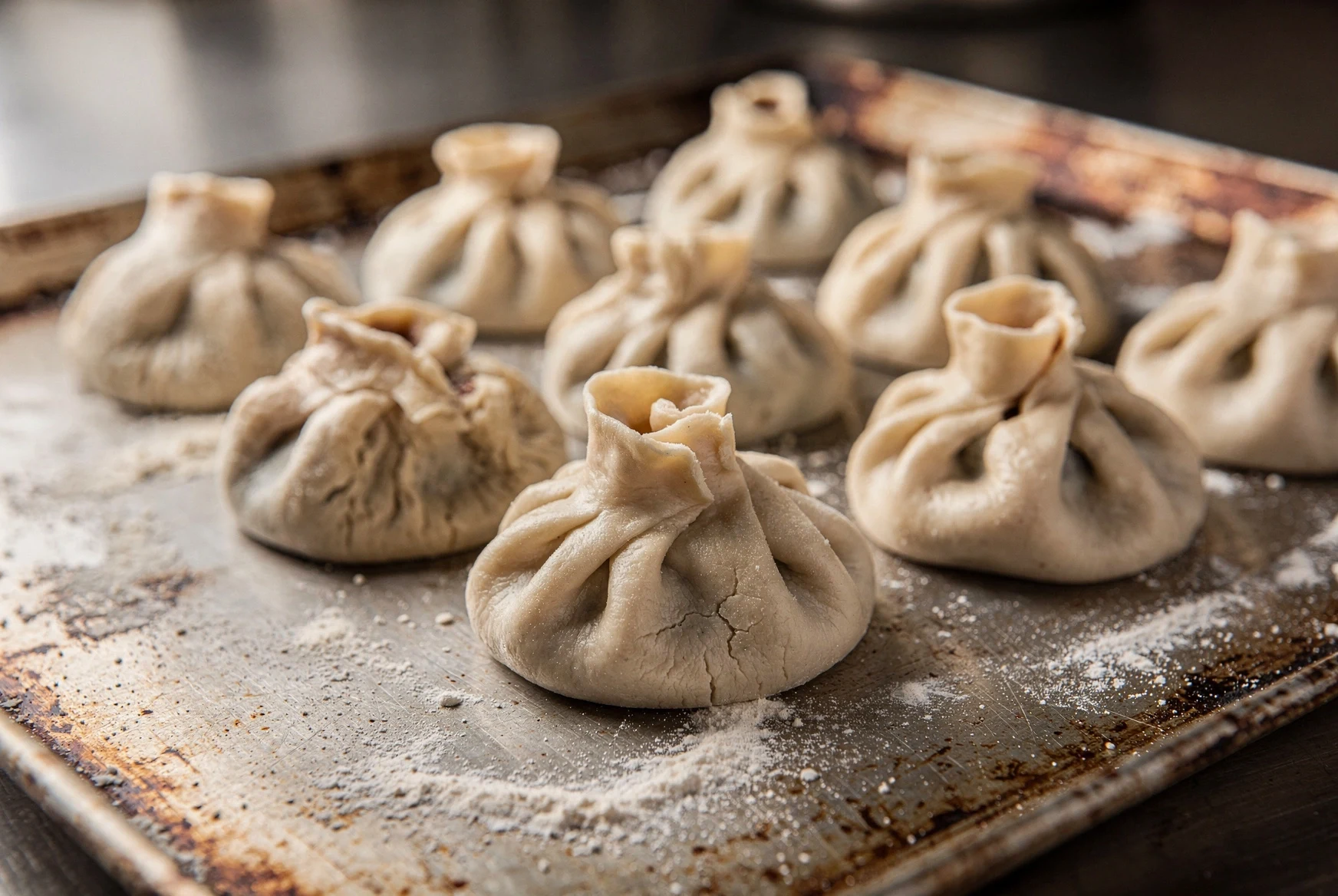 Close-up of freshly folded Georgian khinkali dumplings on a floured tray in a restaurant kitchen