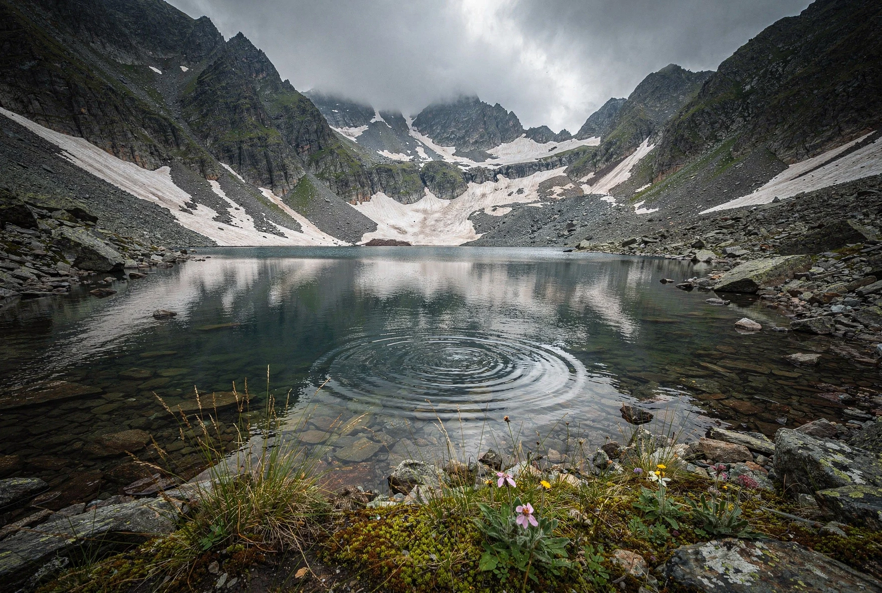 Glacial alpine lake surrounded by dark rocky cliffs and alpine meadows in the Lagodekhi Protected Areas, Greater Caucasus