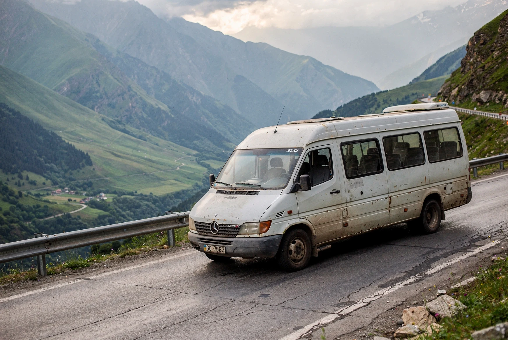 Intercity minibus driving along a mountain road in Georgia under soft afternoon light