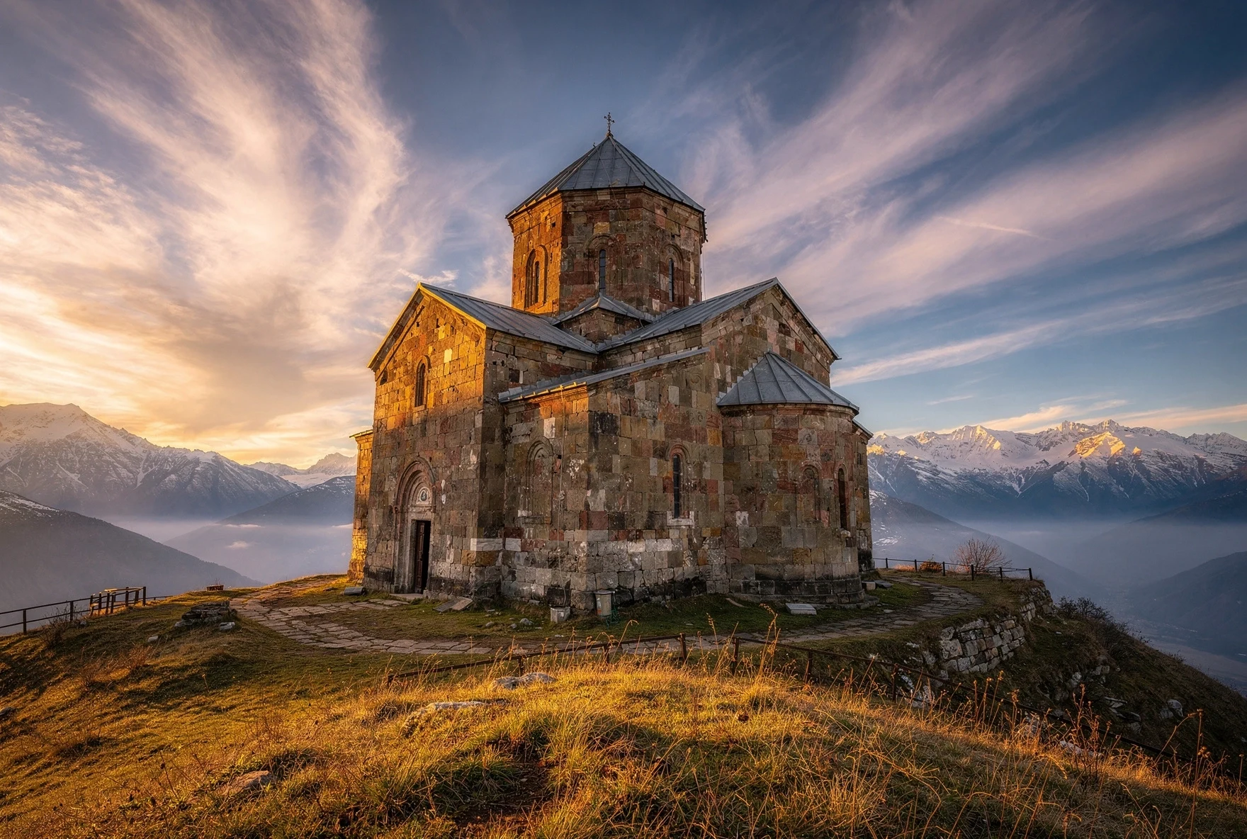 Ancient stone church on hilltop at sunrise with Greater Caucasus mountains and dramatic clouds