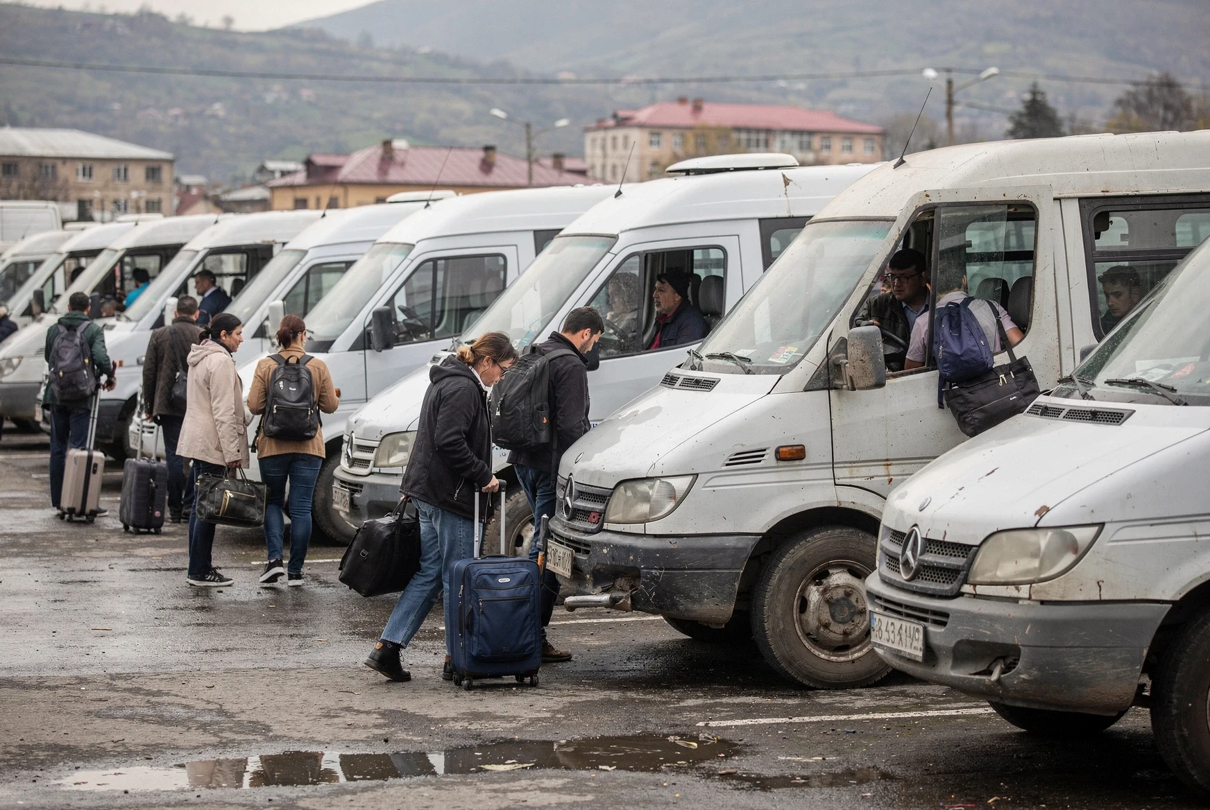 Rows of white intercity minibuses and travelers boarding at a busy Tbilisi terminal