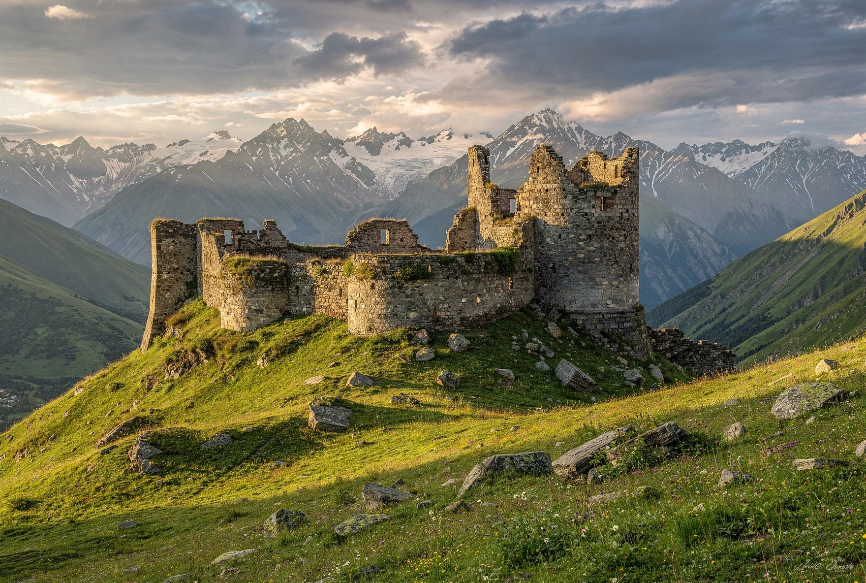 Ruins of a stone fortress on a hilltop in Truso Valley with snow-capped Caucasus mountains in the background