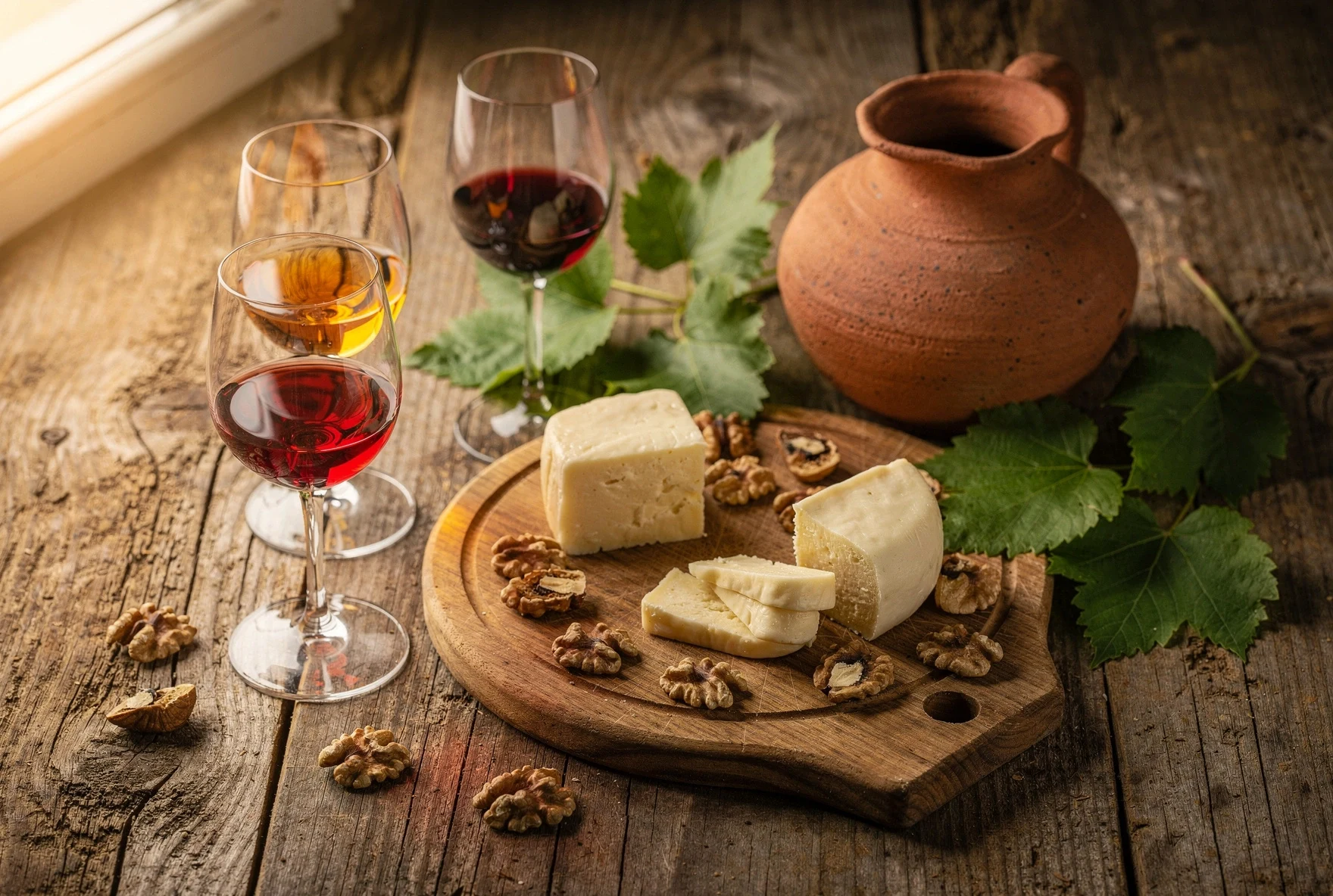Georgian wine tasting setup with glasses of amber, red, and white wine alongside cheese and walnuts