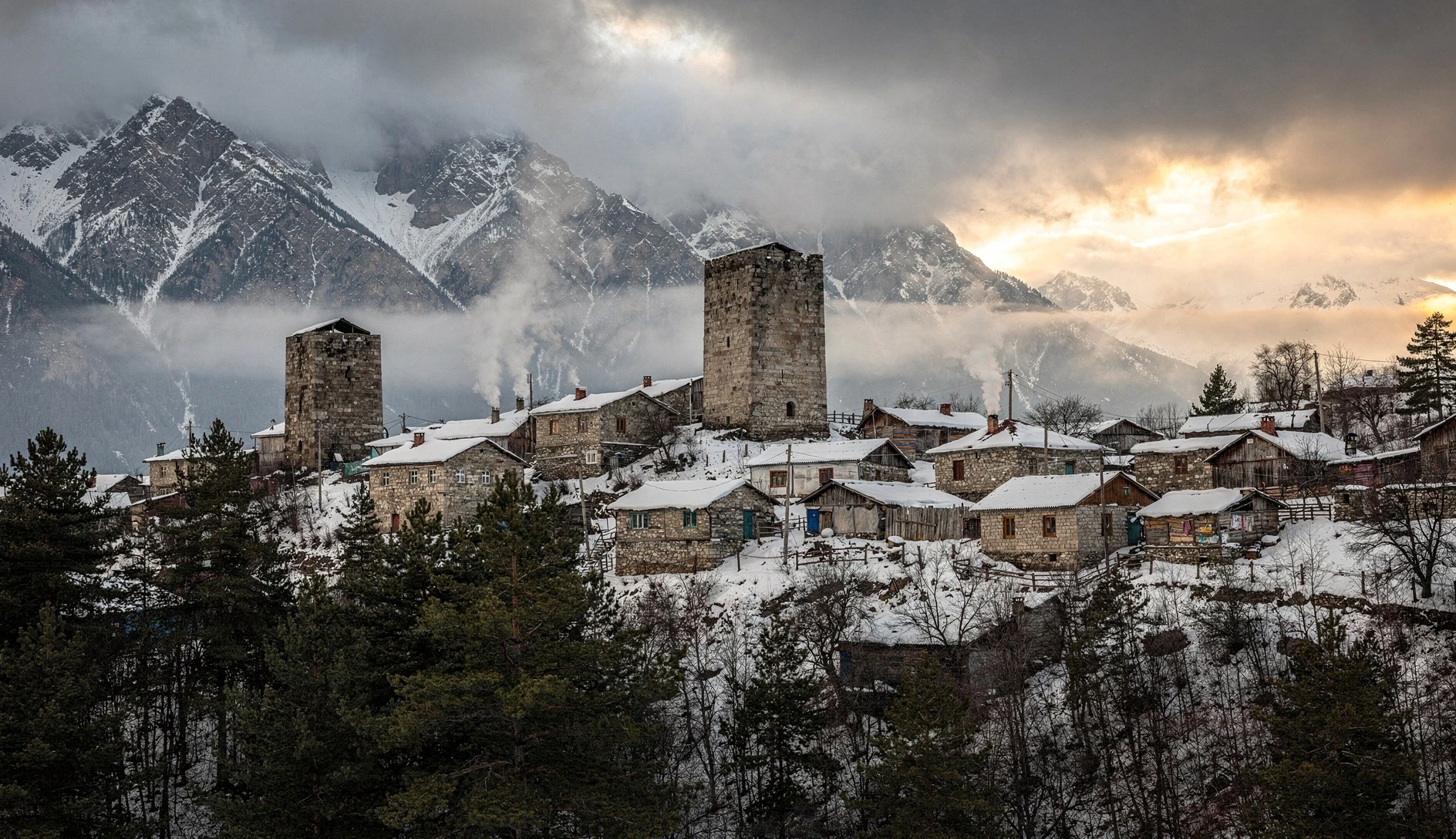 Snow-covered Svan towers in a mountain village in Upper Svaneti, Georgia, with Greater Caucasus peaks in the background